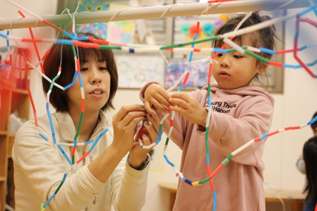 子どもが紐にたくさんのストローを通して遊んでいる様子