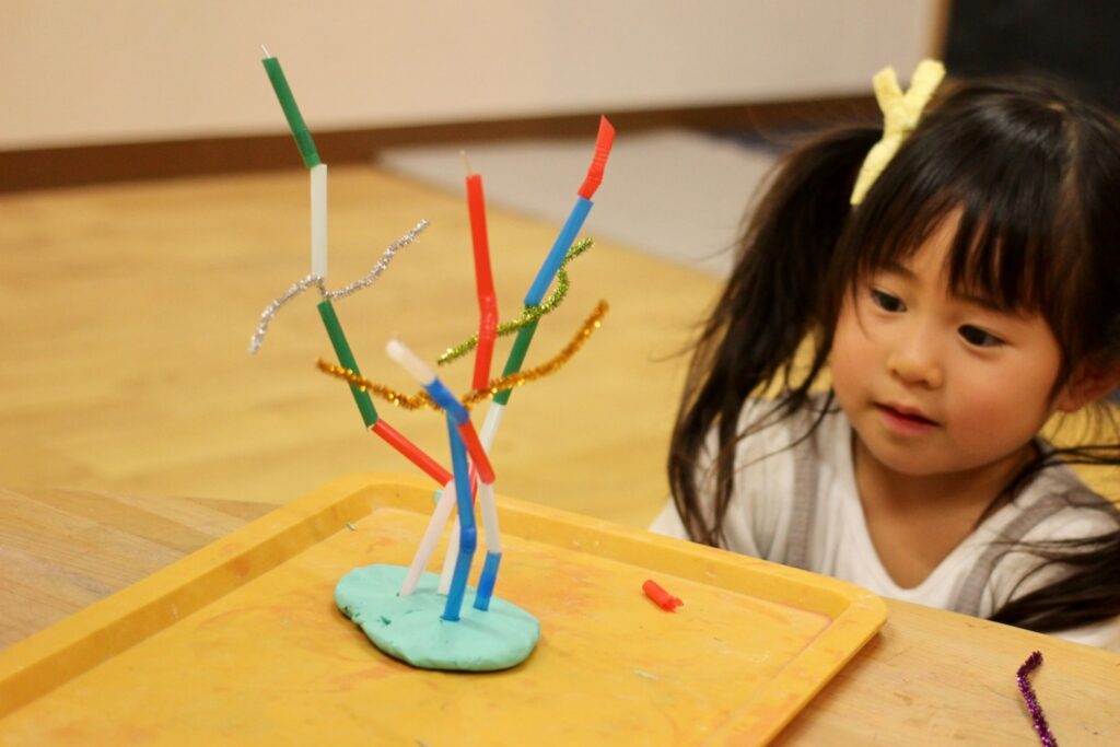 子どもがストローとワイヤーと粘土を使って遊んでいる様子